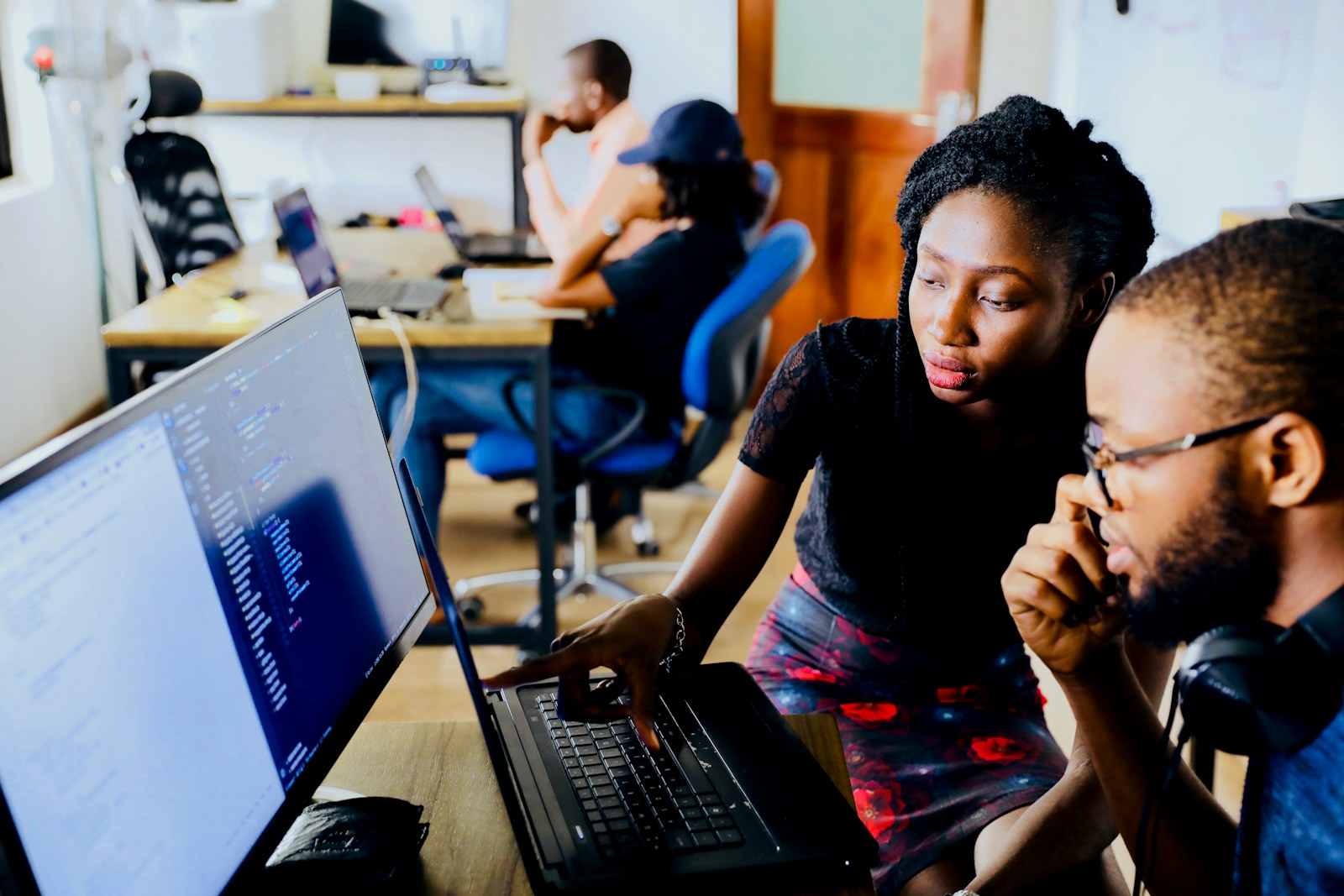 A Black woman and man working together at a laptop in a bright office