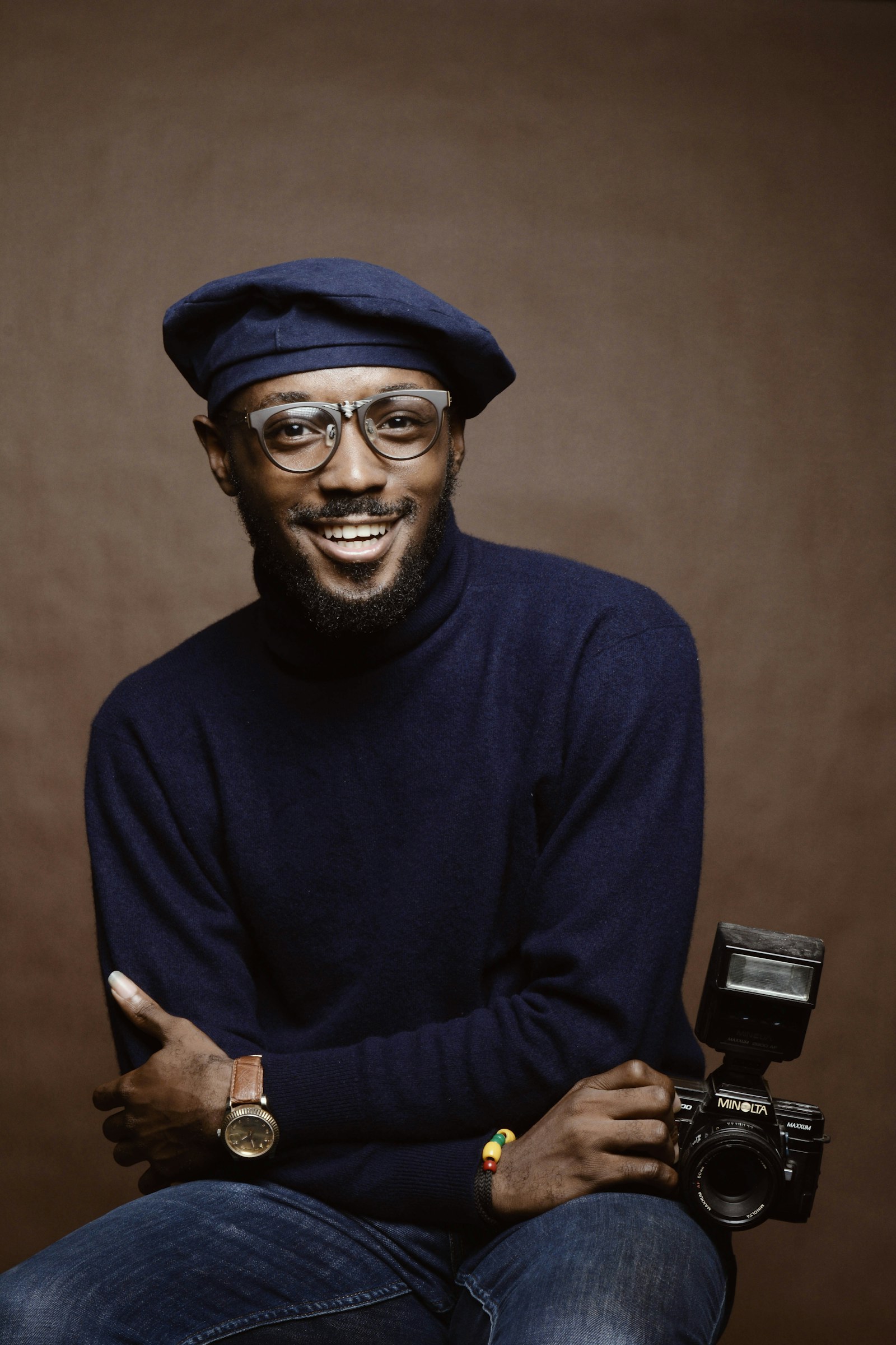 Portrait of a smiling Black man in a navy turtleneck holding a camera